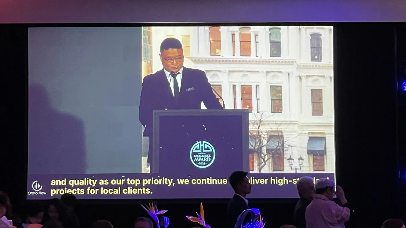 An award recipient speaking Chinese on the main screen at the NZCBIA Excellence Awards, with Orato Flow’s live English captions overlaid along the bottom of the picture.