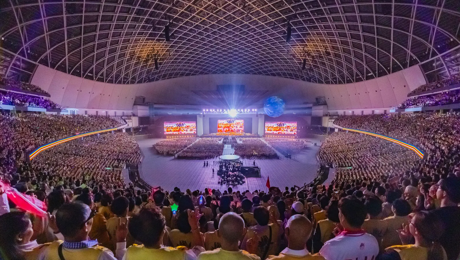 A wide view inside Taipei Dome during the convention: tens of thousands of attendees in the stands and on the floor, facing a stage with three large screens under the dome’s lattice roof.